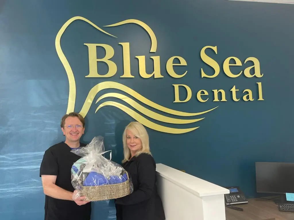 Two people holding a basket in front of the blue sea dental sign.