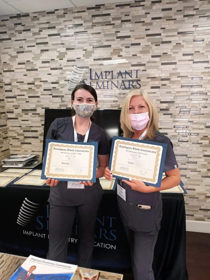 Two women holding certificates in front of a wall.