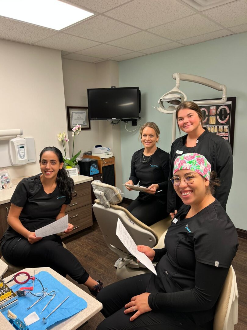 Four women sitting in a dental office smiling for the camera.