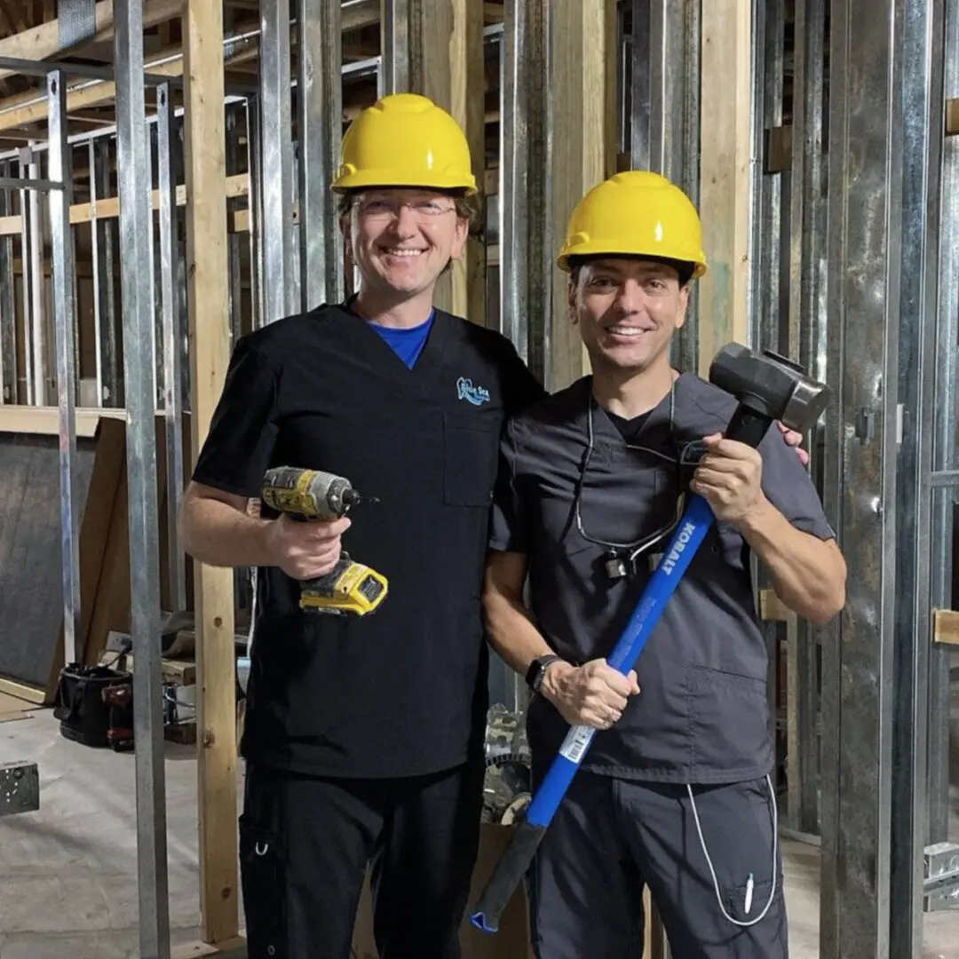 Two men in hard hats standing next to a wall.