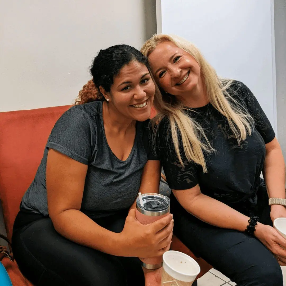 Two women sitting on a couch with drinks.