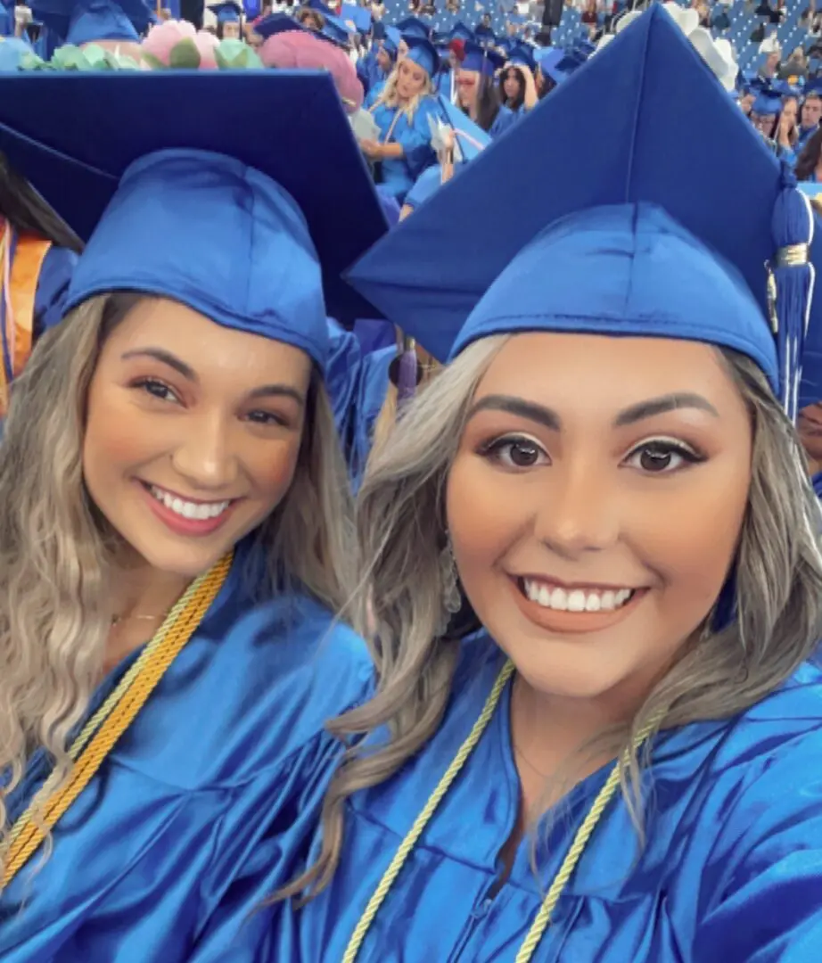 Two women in blue caps and gowns posing for a picture.