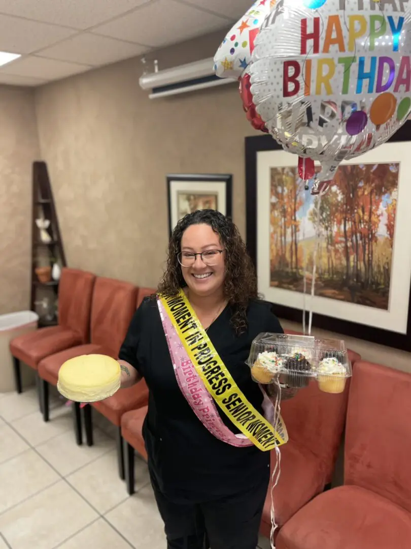 A woman holding a cake and wearing a birthday sash.