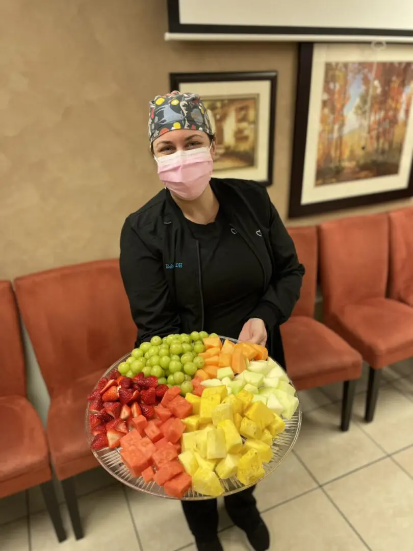 A woman holding a bowl of fruit in front of her face.