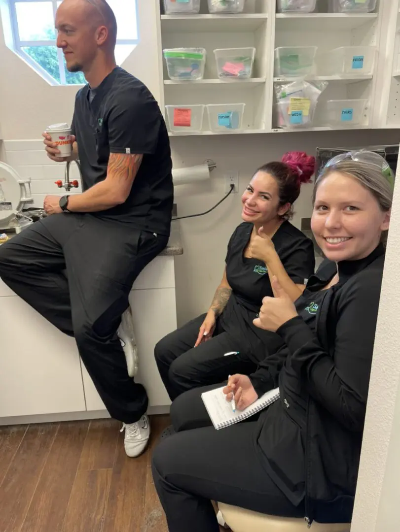 Three people sitting in a room with one holding up the thumbs.