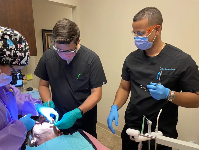 Two people in black shirts and blue gloves working on a tooth.