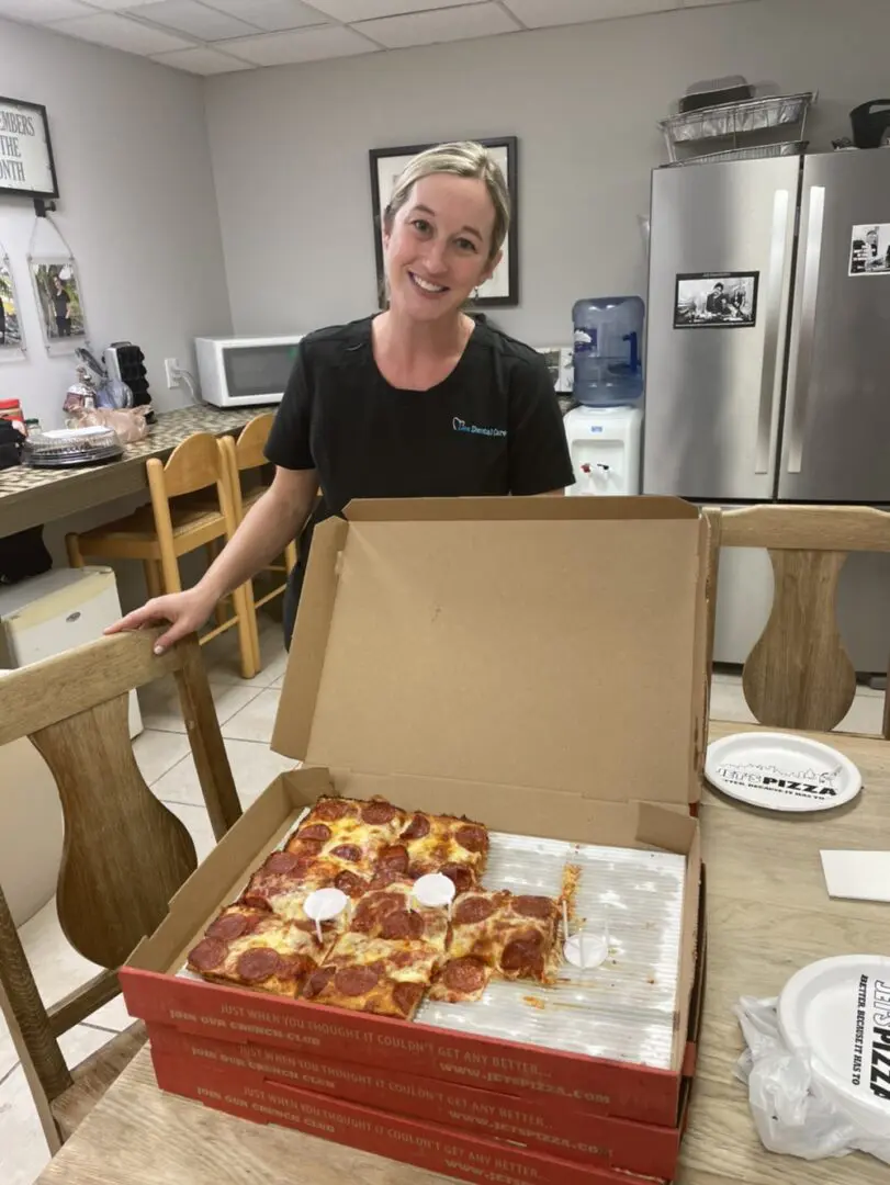 A woman sitting at the table with a box of pizza.