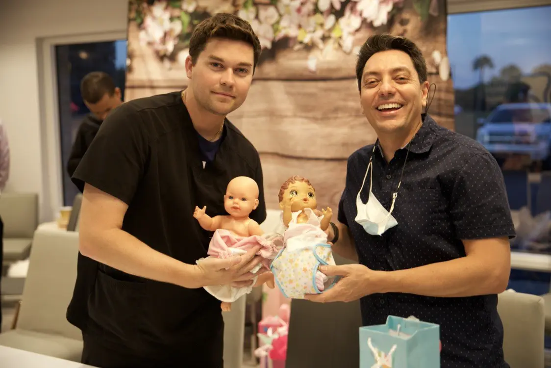 Two men holding baby dolls and a gift bag.