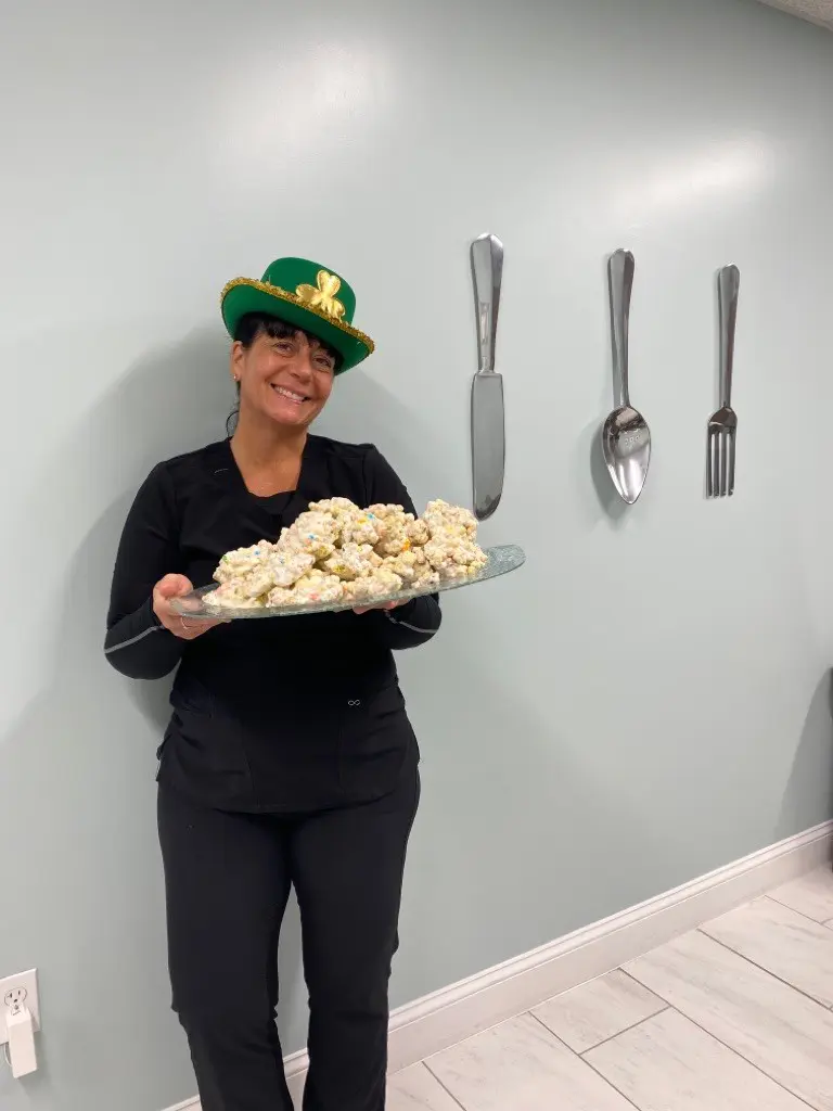 A woman holding a tray of donuts in front of wall.