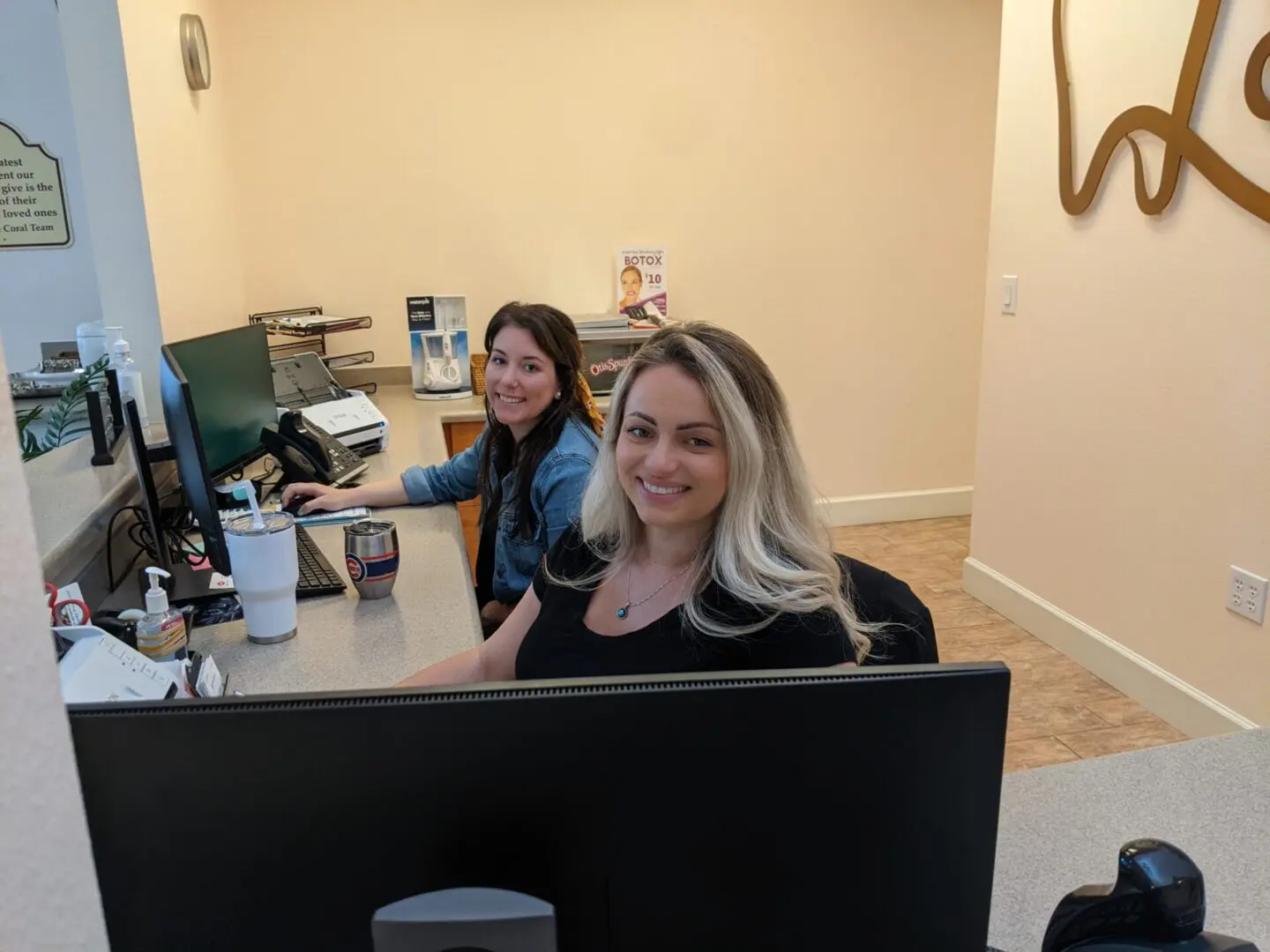 Two women sitting at a computer desk smiling for the camera.