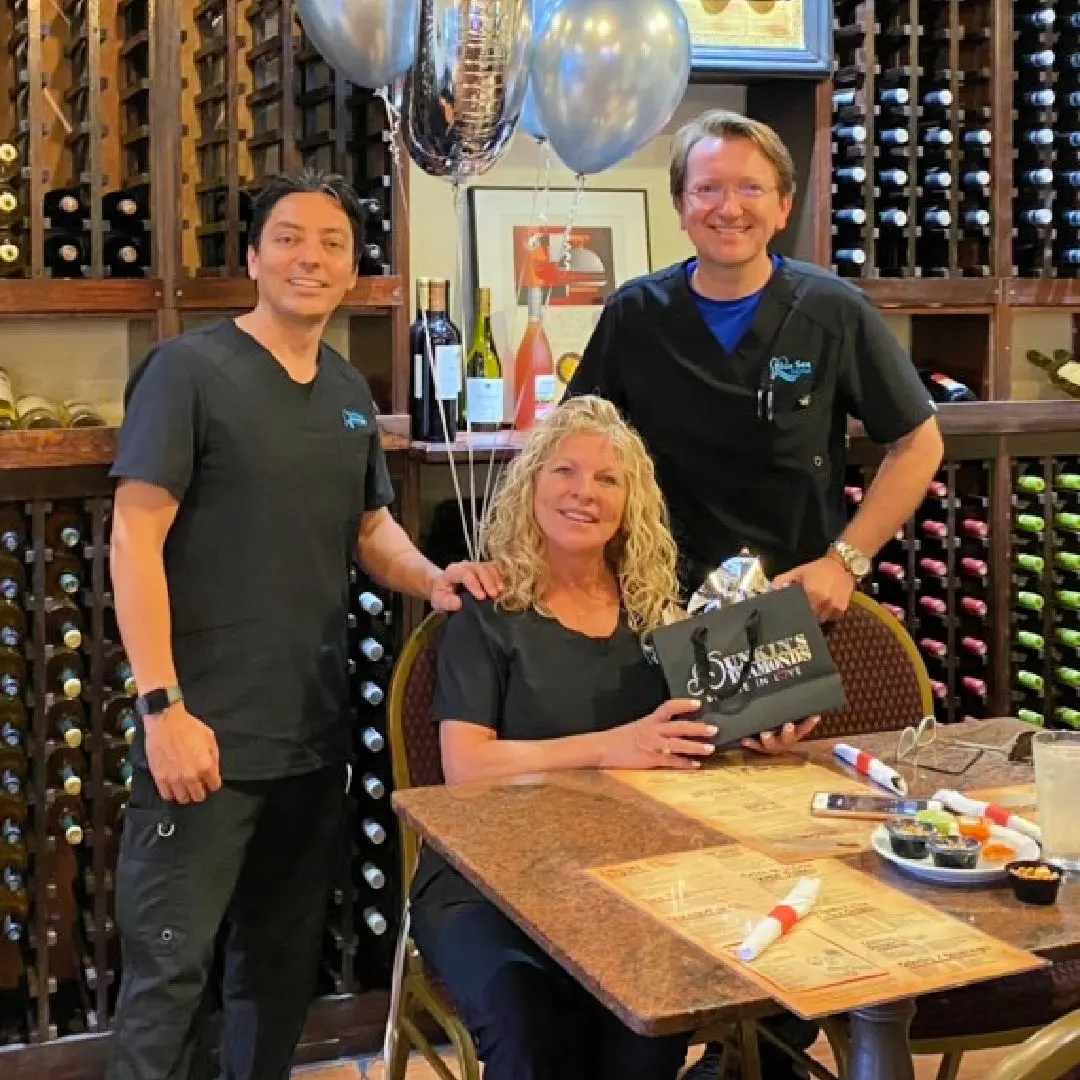 Three people posing for a picture in front of wine bottles.