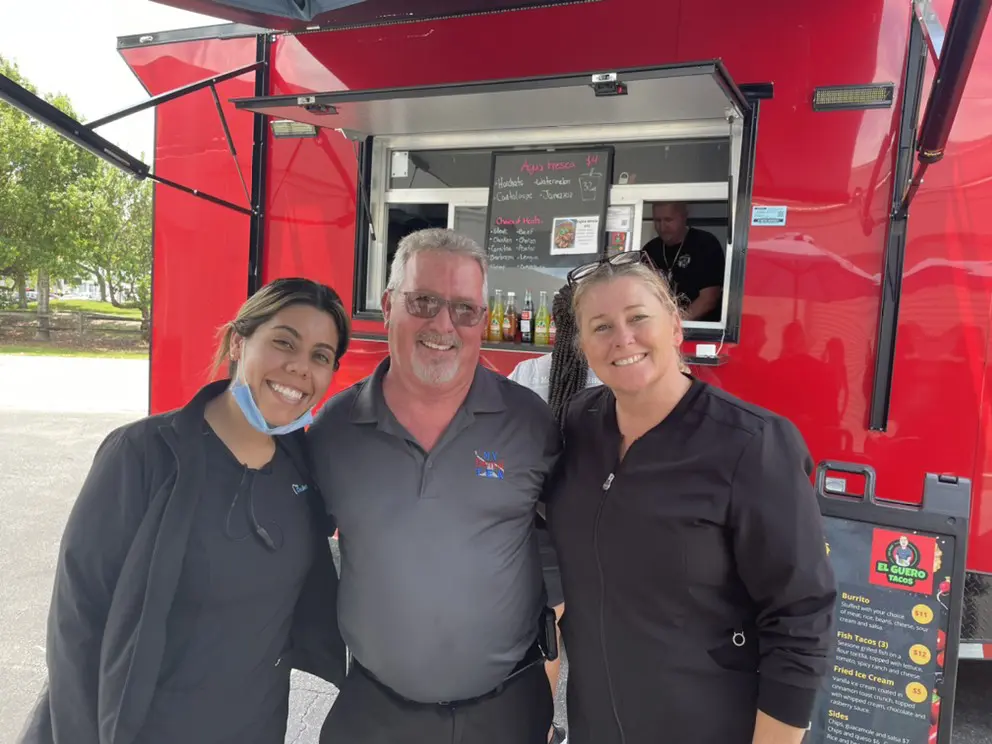 Three people standing in front of a food truck.