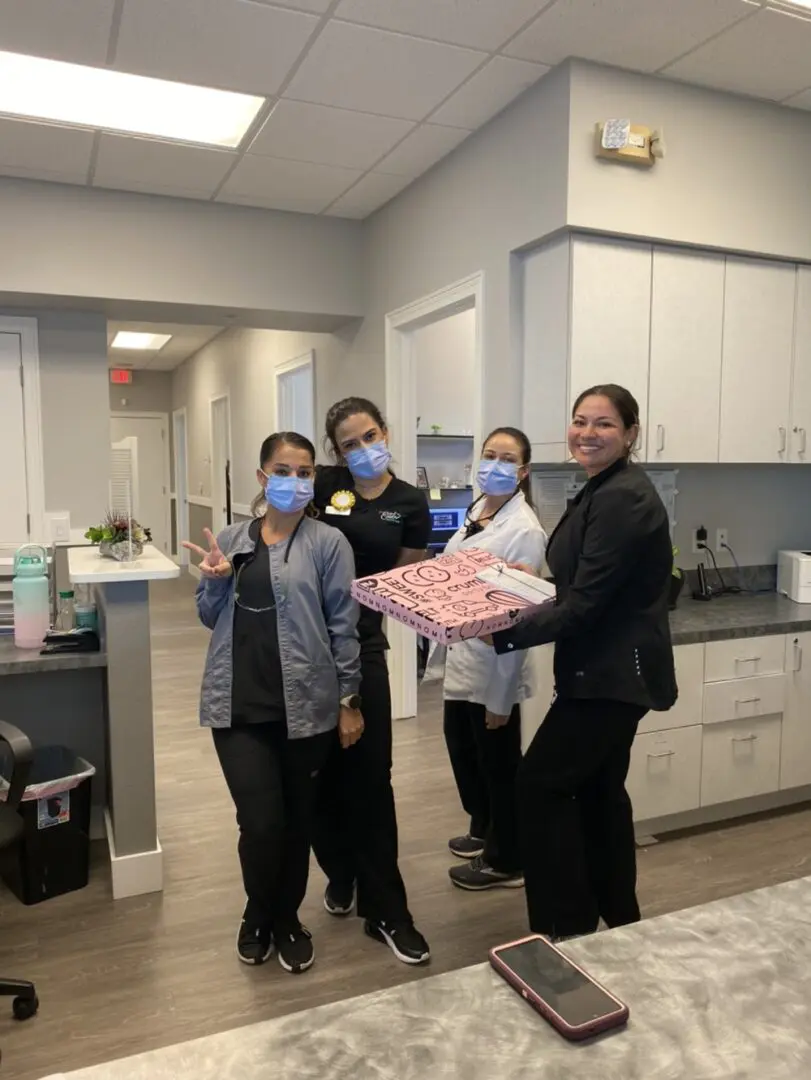 Four women in a dental office holding up their hands.