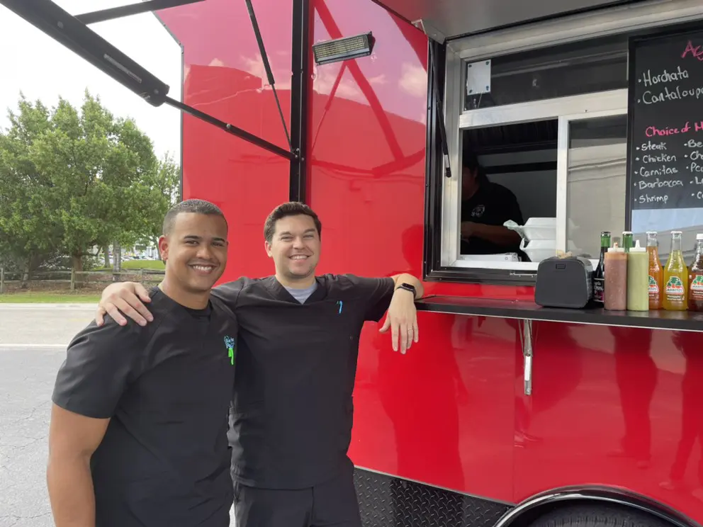 Two men standing next to a food truck.