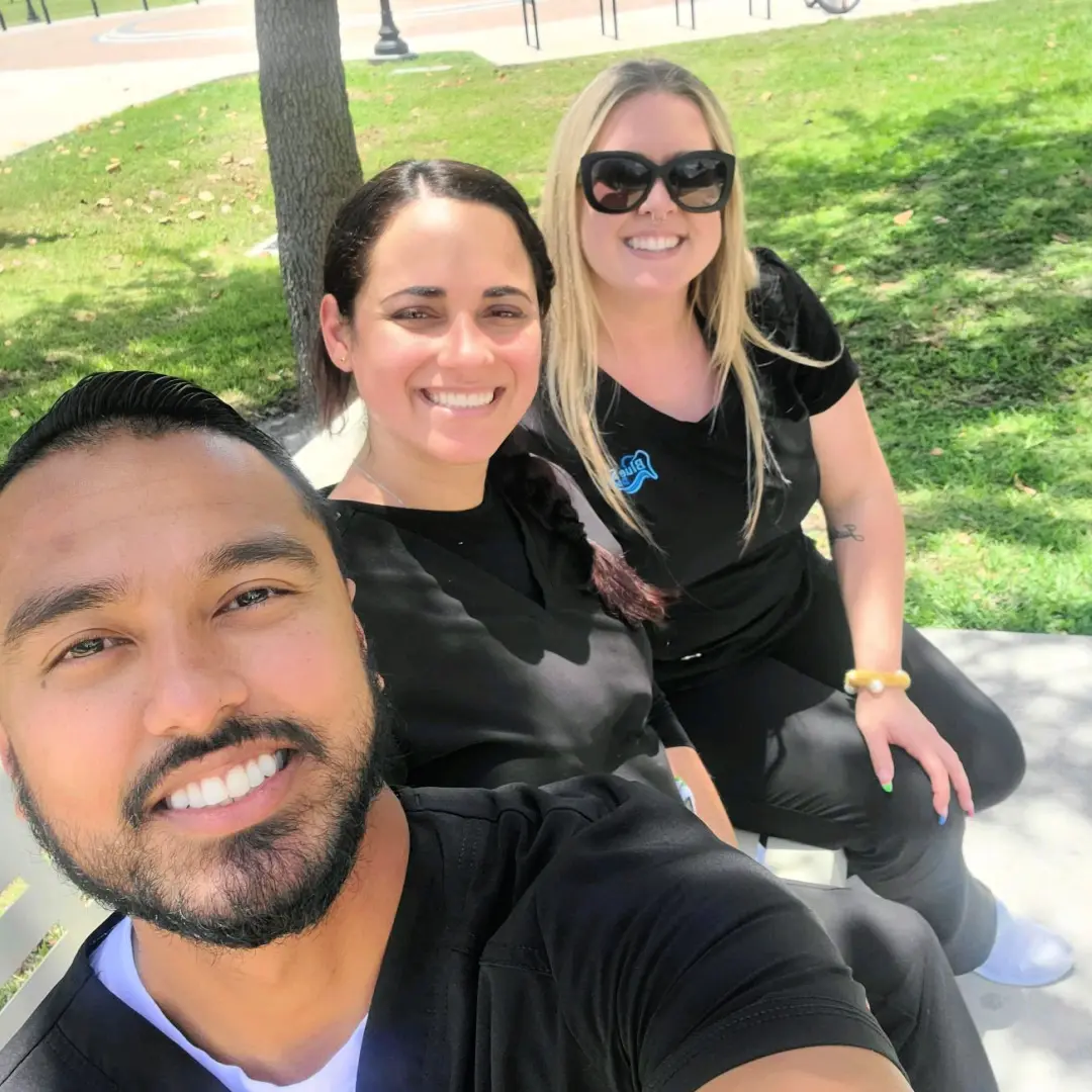 Three people sitting on a bench smiling for the camera.