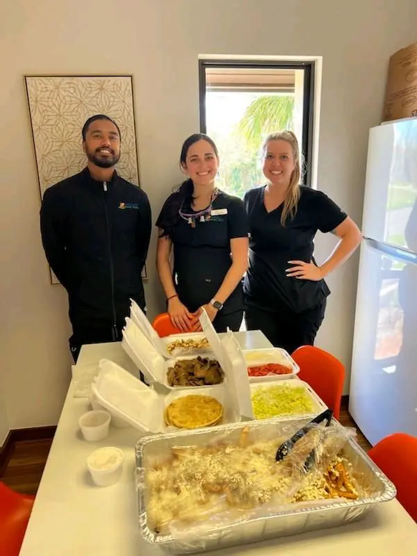 Three people standing in front of a table with food.