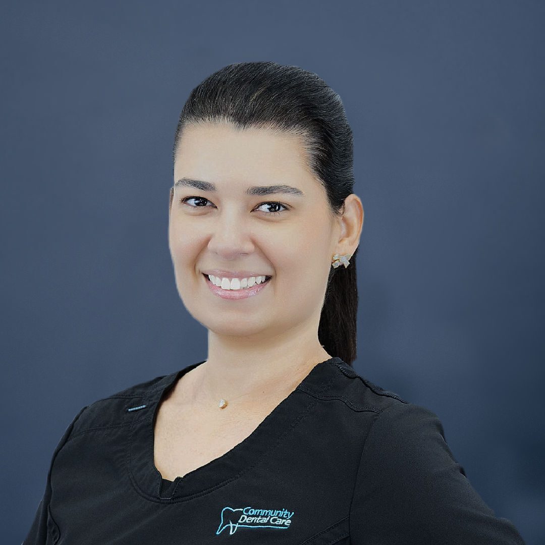 Female dentist with dark hair wearing scrubs smiliing