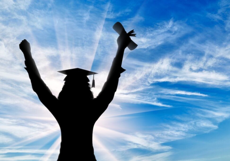 A person in graduation cap and gown holding up their arms.