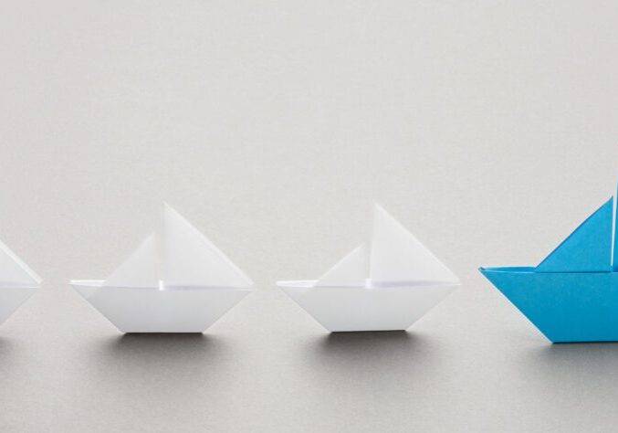 A blue paper boat is in front of two white boats.