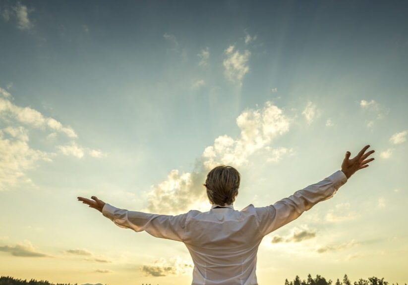 A man with his arms outstretched in front of the sky.